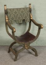 A heavily carved cross x frame chair with painted finish, leather seat and upholstered tapestry