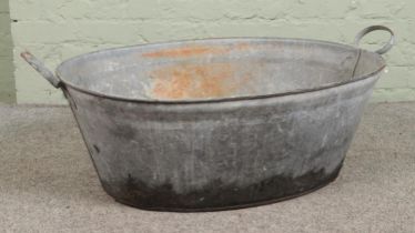 An oval galvanised tin bath, with twin handles. Height: 32cm, Width: 102cm.