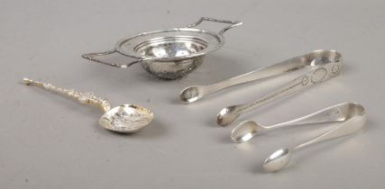 Four silver utensils, to include sugar tongs, tea strainer and decorative spoon. Total weight: 82g