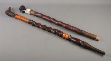 Two tribal style walking sticks both with carved detail depicting tribesmen one with cow horn detail