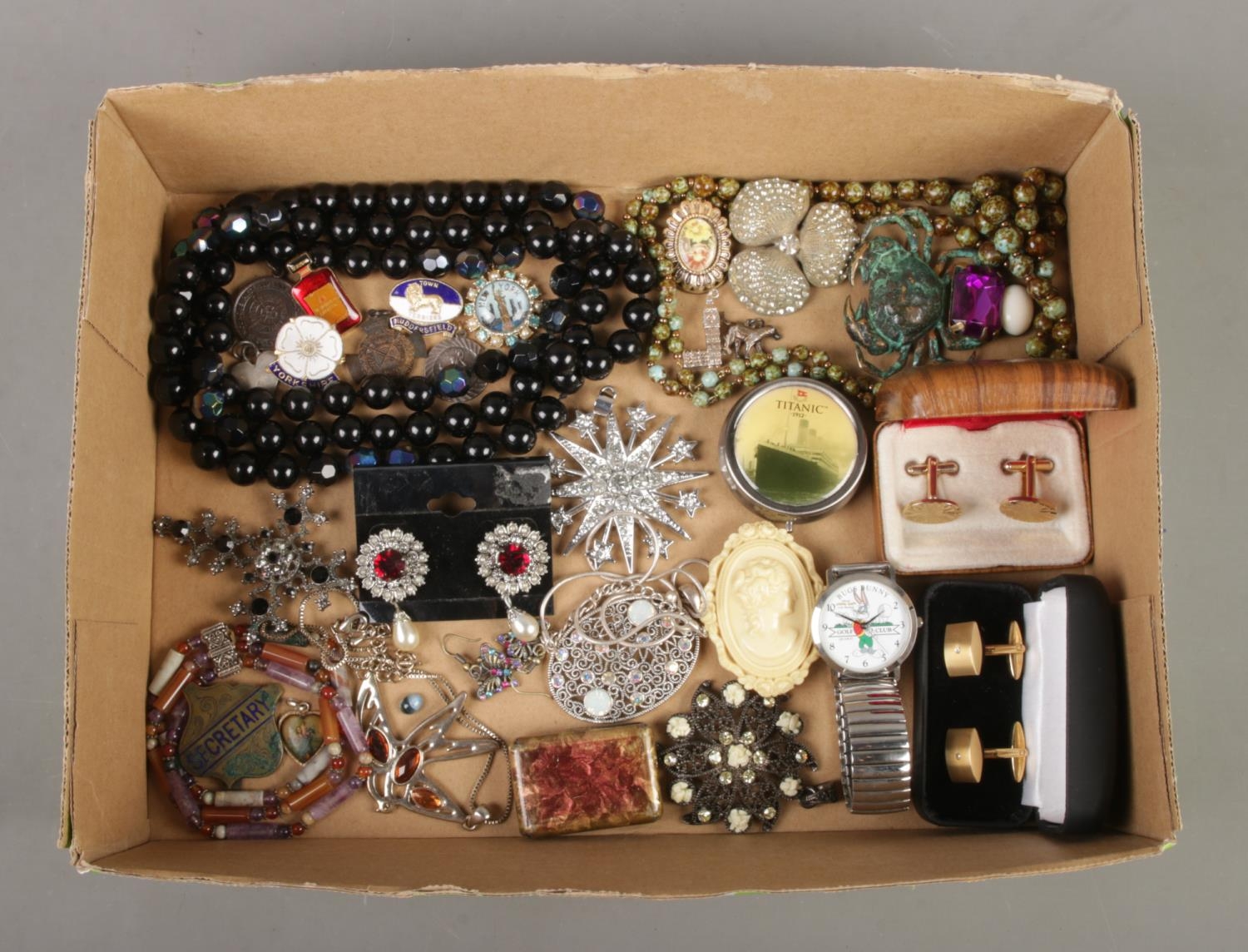 A box containing an assortment of costume jewellery. To include white metal big ben and dog