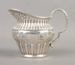 An early Twentieth Century silver cream jug, heavily engraved with floral detailing to the central