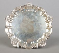 A late Victorian silver pin tray, with scrolled and shell decoration to the rim, raised on three