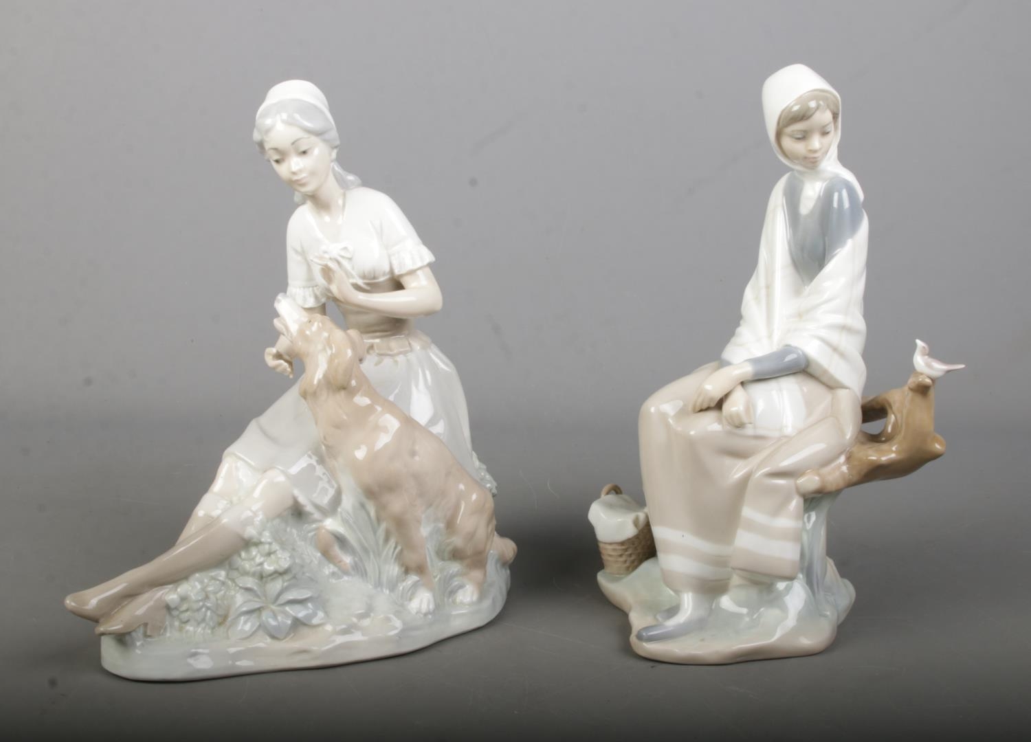Two Nao by Lladro ceramic figures each depicting seated maidens interacting with animals.