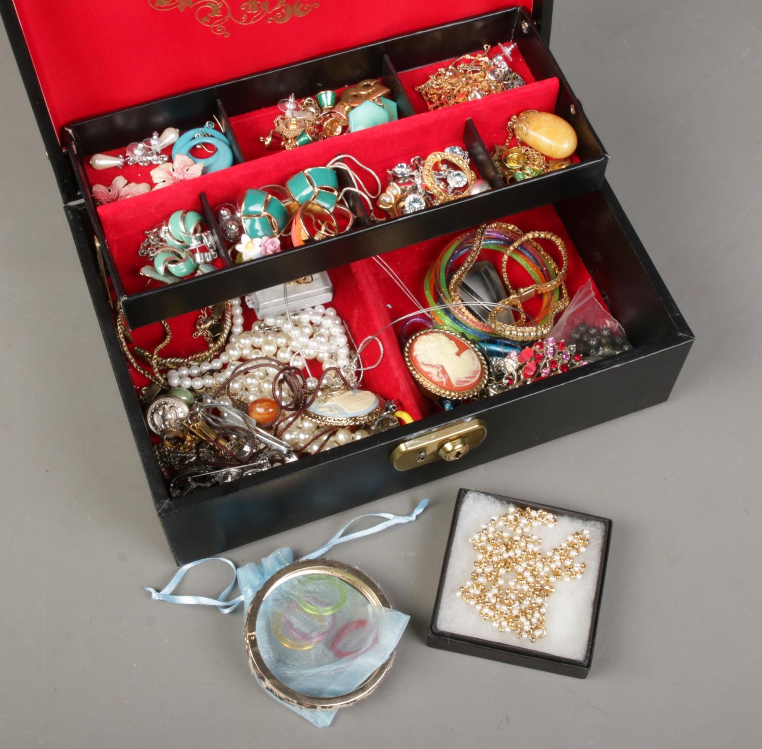 A jewellery case with contents of costume jewellery. Includes enamel earrings, simulated pearls,