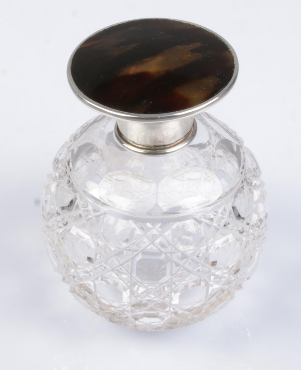 A globular cut glass scent bottle with silver and tortoise shell top.