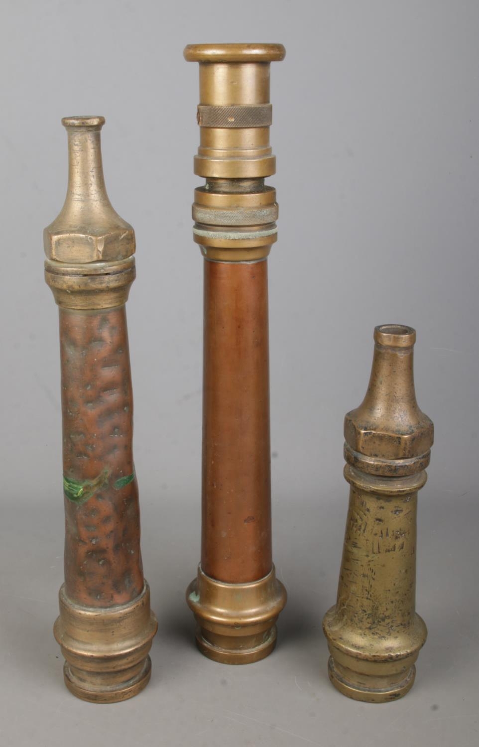 Three antique brass and copper fire hose nozzles of varying sizes. Largest example length 49cm.