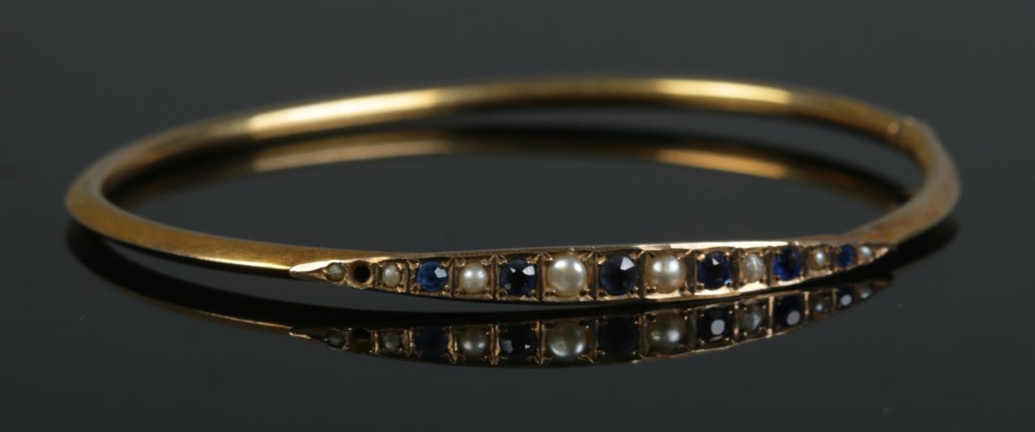 A 9ct Gold bangle, set with sapphire coloured stones and pearls. Total weight: 3.5g One stone