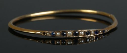 A 9ct Gold bangle, set with sapphire coloured stones and pearls. Total weight: 3.5g One stone