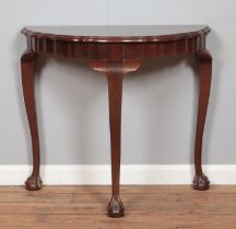 A mahogany demi-lune console table, with waved edging and three ball and claw feet. Bearing label