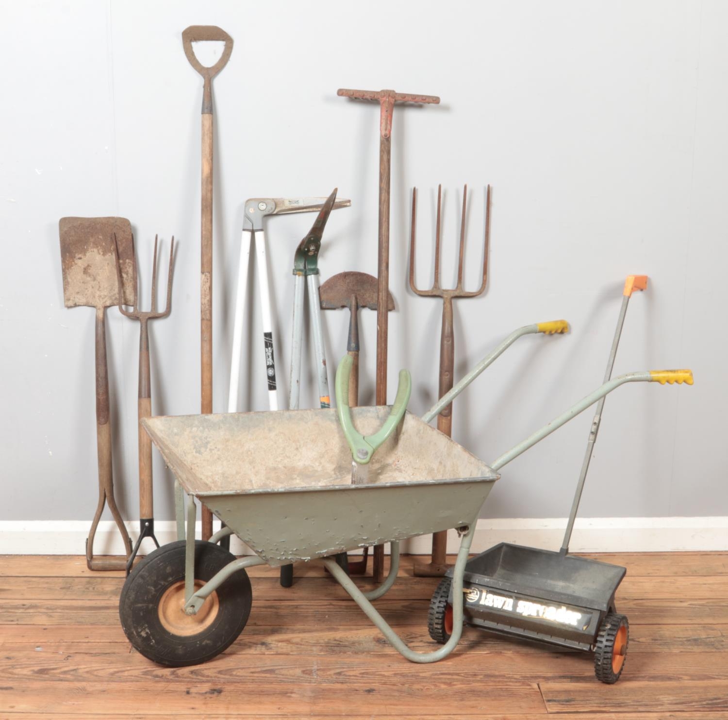 A collection of garden tools. Includes wheel barrow, lawn spreader, Wilkinson Sword etc.