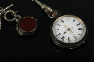 A white metal fob watch with Roman Numeral dial, suspended on silver albert chain featuring T-Bar,