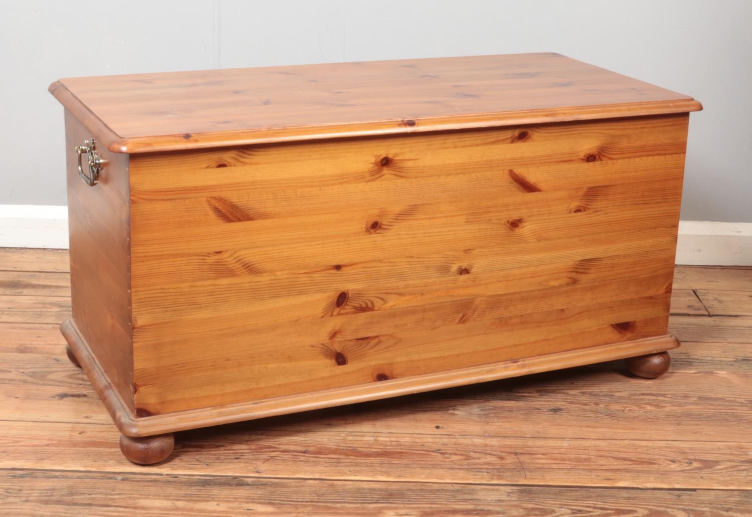 A pine blanket box raised on ball feet featuring decorative brass handles. Approx. dimensions