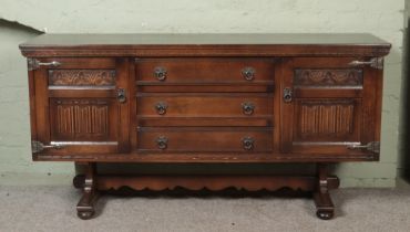 An old charm oak carved sideboard with linen fold detail on doors flanking three drawers.