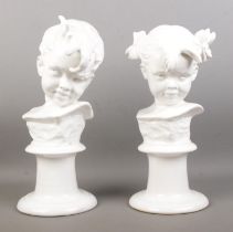 A pair of white glazed ceramic busts, depicting a boy and girl. Raised on turned stepped bases.