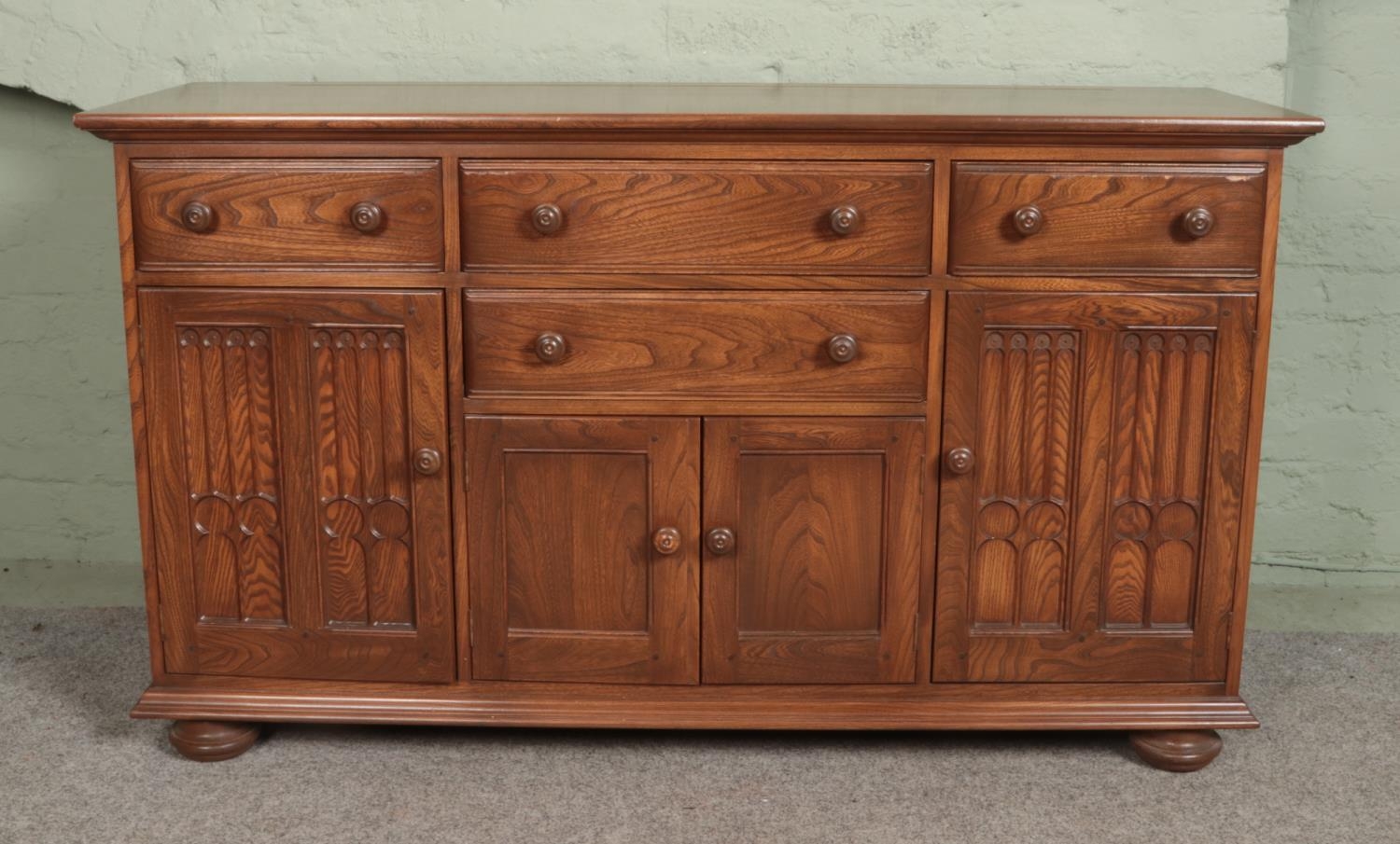 An Ercol elm Canterbury dresser base having a combination of four drawers and three cupboard doors