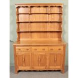 An Ercol light oak Welsh dresser, with cupboard doors and drawers to the base and plate rack top.