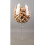 A large wine glass with contents of corks. Height of glass 49.5cm.