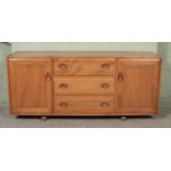 An Ercol light elm Windsor sideboard with three drawers flanked by cupboard doors. The top drawer