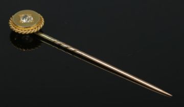 A gold stick pin set with a single diamond and having rope twist border. Tests as high carat.