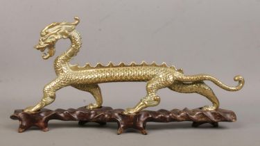 A brass figure of a Chinese dragon raised on hardwood stand. Height 16cm, Length 34cm.