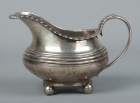 An early 19th century silver cream jug. With gadrooned rim and raised on four ball feet. Assayed