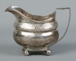 A Georgian silver cream jug with engraved decoration and raised on four ball feet. Bearing London