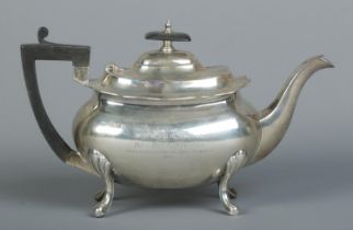 A George V silver teapot. Raise on four scrolling feet and having ebonised finial and handle.