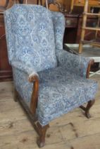 An upholstered and showwood wing armchair, the arms carved with parrots heads