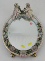 A Continental porcelain encrusted oval mirror, decorated with putti and flowers, with easel support,