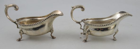 A pair of silver sauce boats, with gadrooned edge, scroll handle and raised on three scroll legs,