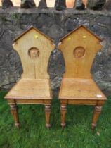 A pair of 19th century oak hall chairs, with shield to the carved solid back, solid seat, on