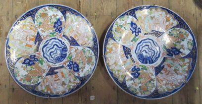 A pair of large Japanese Imari chargers, decorated with sectional scenes of gardens and figures to a