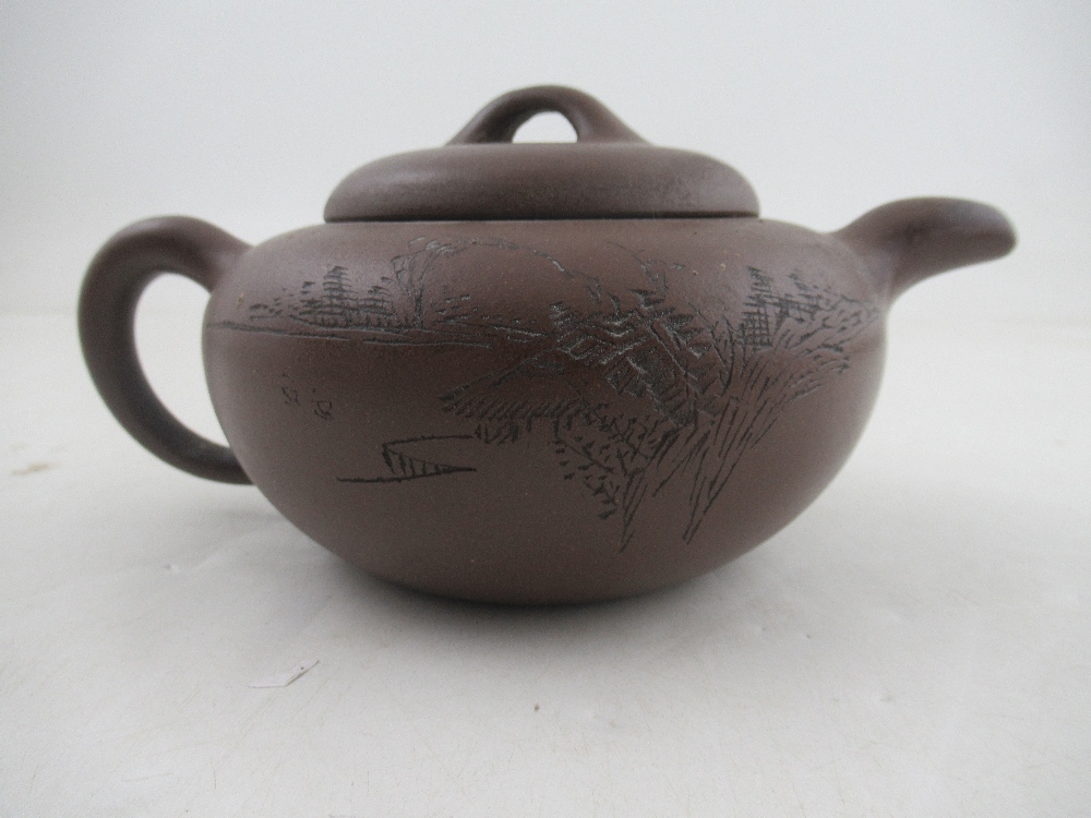 A Chinese Yixing style terracotta teapot, incised with a landscape and script, with seal mark,