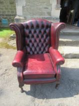 A Thomas Lloyd red leather wing back armchair, with deep buttoned back, raised on claw on ball feet