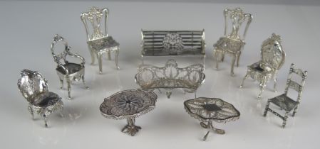 A collection of silver miniature furniture including garden bench, two filigree tables, filigree