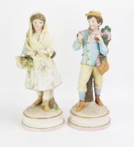 A large pair of late 19th century German bisque porcelain figures of a boy and girl carrying