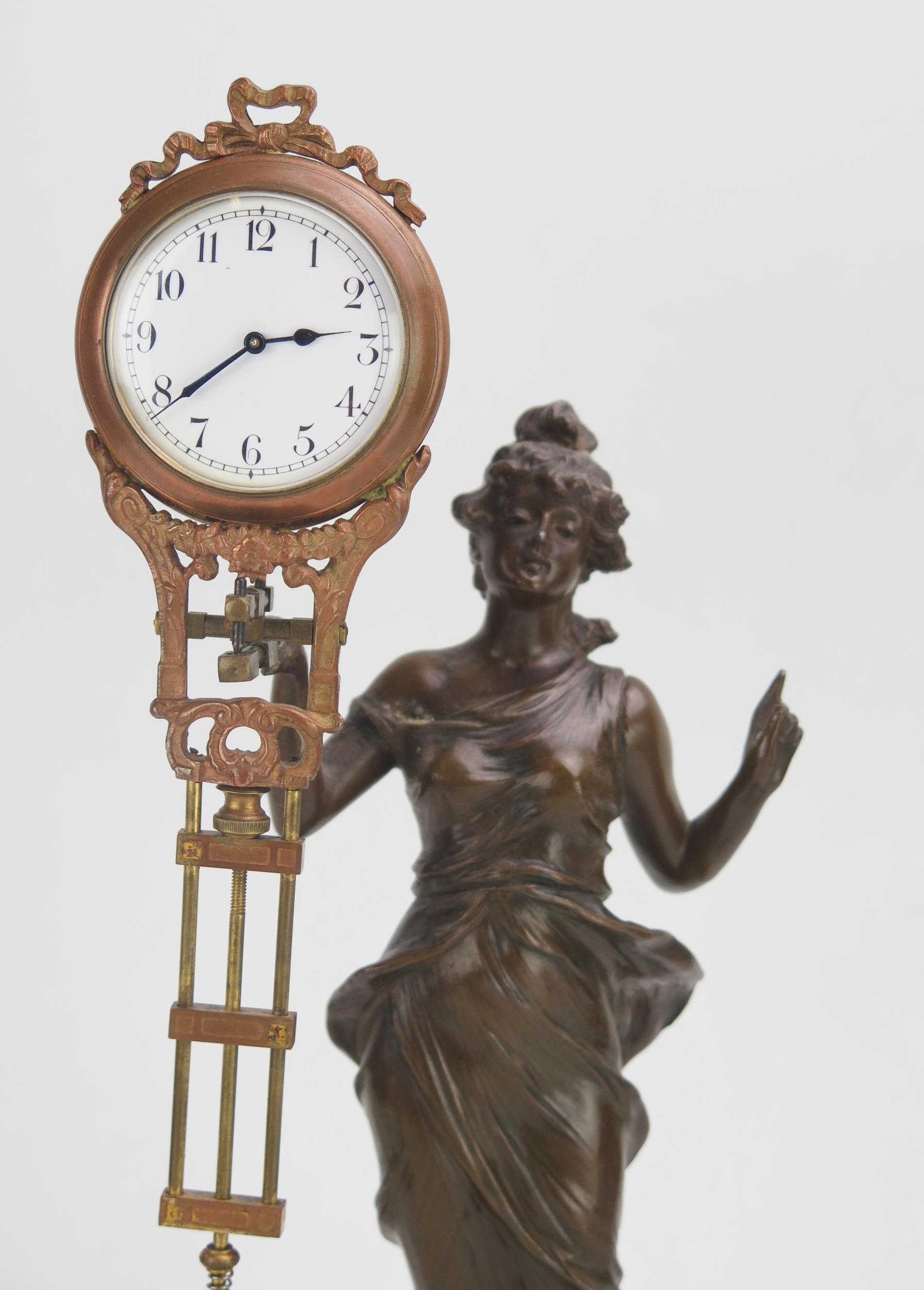 A bronzed metal mystery timepiece, modelled as a young lady standing in a flowing dress holding - Bild 2 aus 3