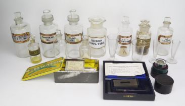 A collection of clear glass pharmaceutical bottles and stoppers, measuring jars, syringe etc.
