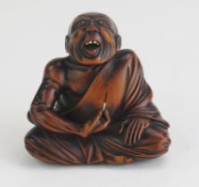 A Carved hardwood netsuke of a professional sneezer seated with his right hand raised, holding a
