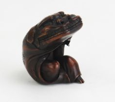 A Japanese carved hardwood netsuke depicting a man putting on a Dragons head costume, unsigned,