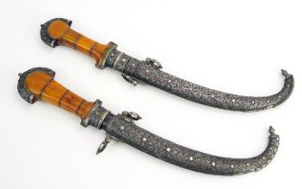 A pair of Moroccan daggers, with 20cm curved double edged blades, silver mounted cross guards,