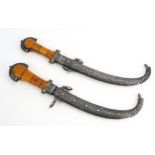 A pair of Moroccan daggers, with 20cm curved double edged blades, silver mounted cross guards,