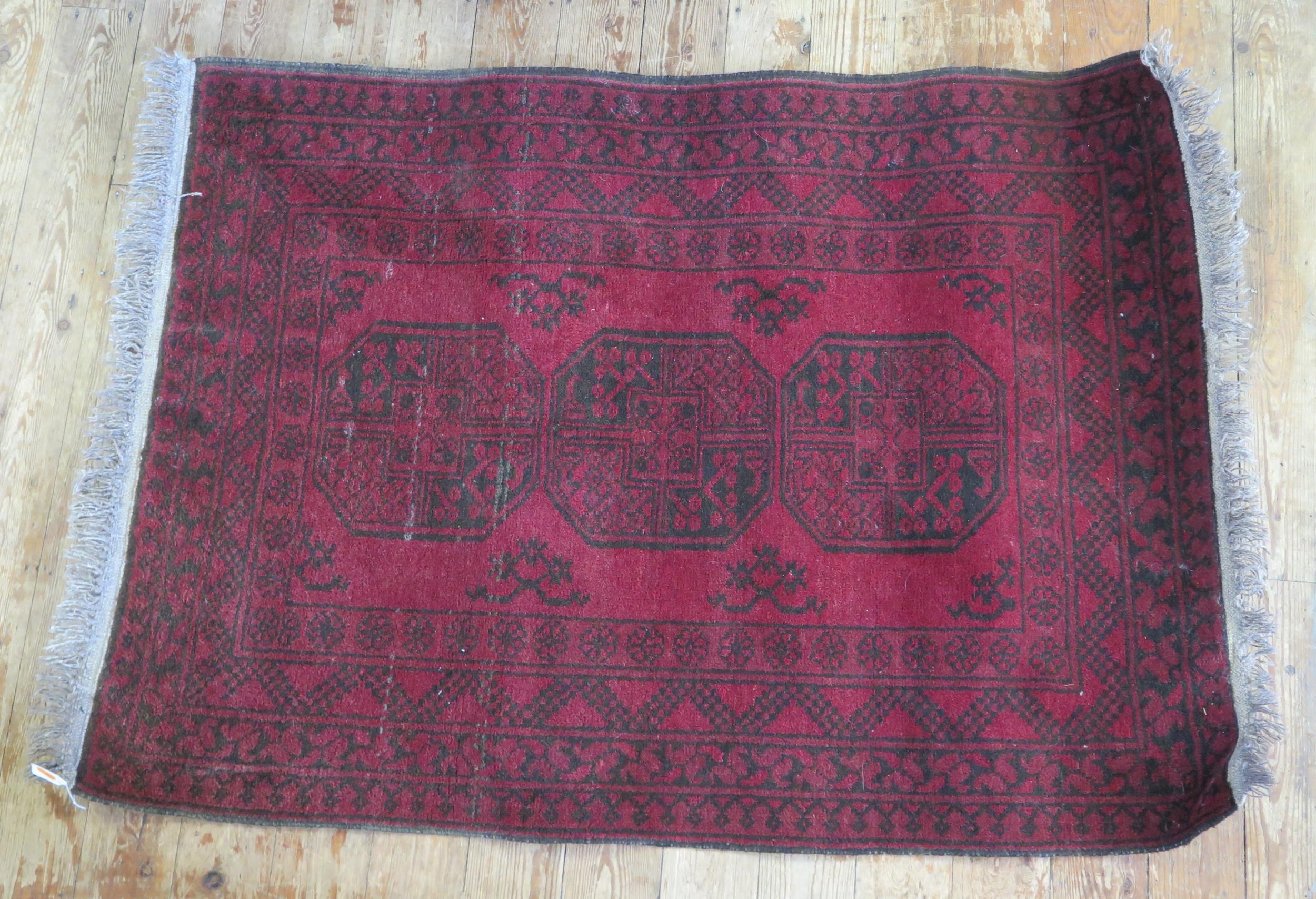 An Afghan rug, the wine red field with single row of three octagonal medallions, within a multiple