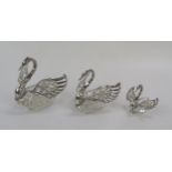Three graduated clear glass and silver mounted table salts in the form of swans, with silver