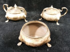 A pair of George V silver circular mustard pots, raised on hoof feet, and a matching salt,