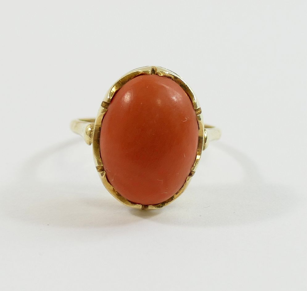 An oval coral cabochon in unmarked yellow metal ring mount, finger size K, 3.7g gross CONDITION