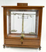 A set of early 20th century brass apothecary/precision scales, housed in glazed wooden case, with