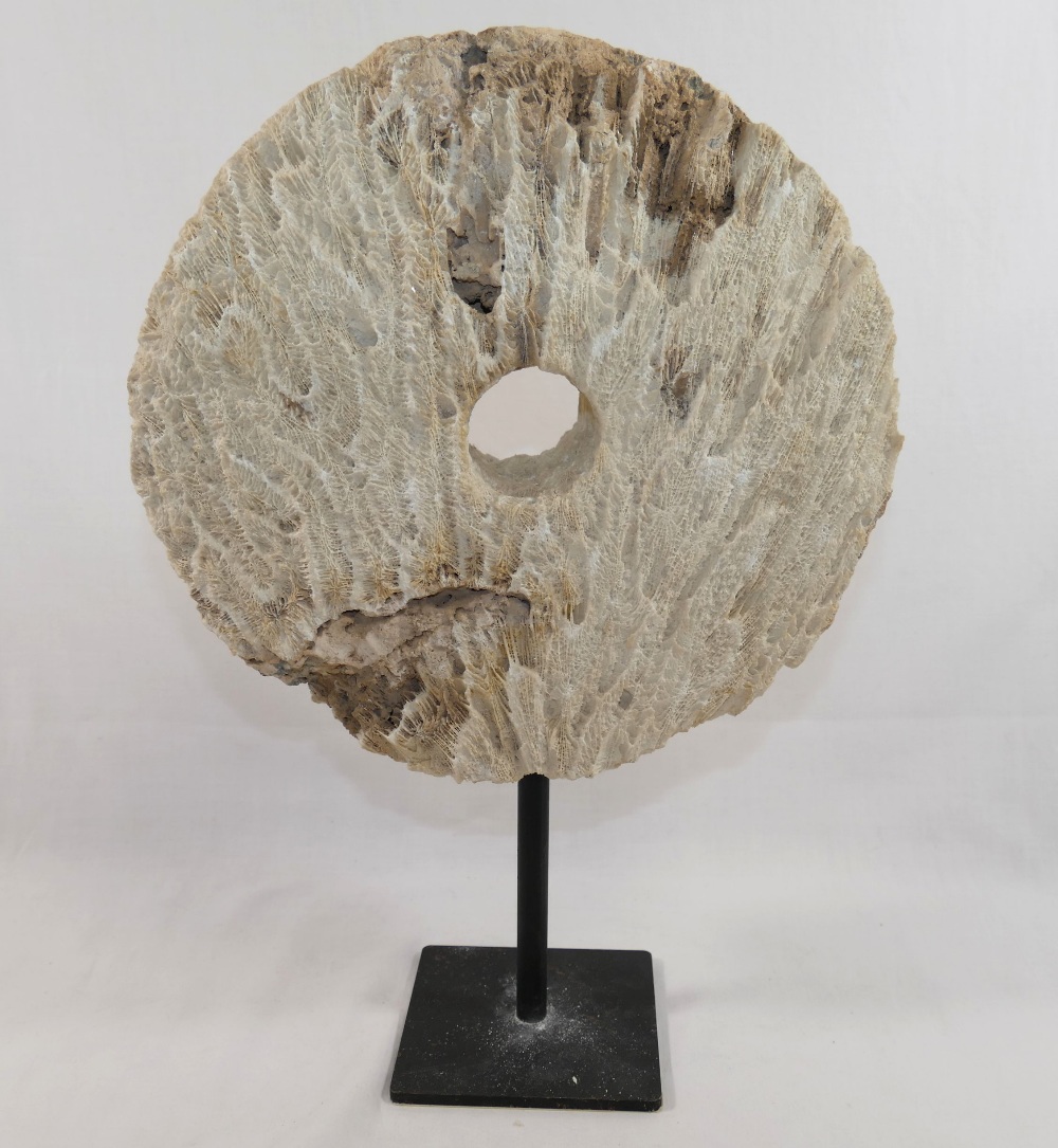 A large coral circular carved disc with central hole, (similar to that of a rai stone), raised on