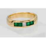 An 18ct yellow gold band channel set ring set with a princess cut diamond and four emeralds, band